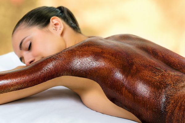 Close up detail of young woman with dark chocolate massage wax applied on back. Girl laying with eyes closed on couch in spa.